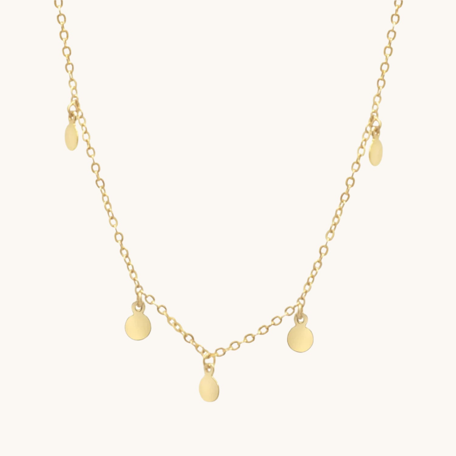 Gold plated boho necklace with small circle drops along its length, on cream background
