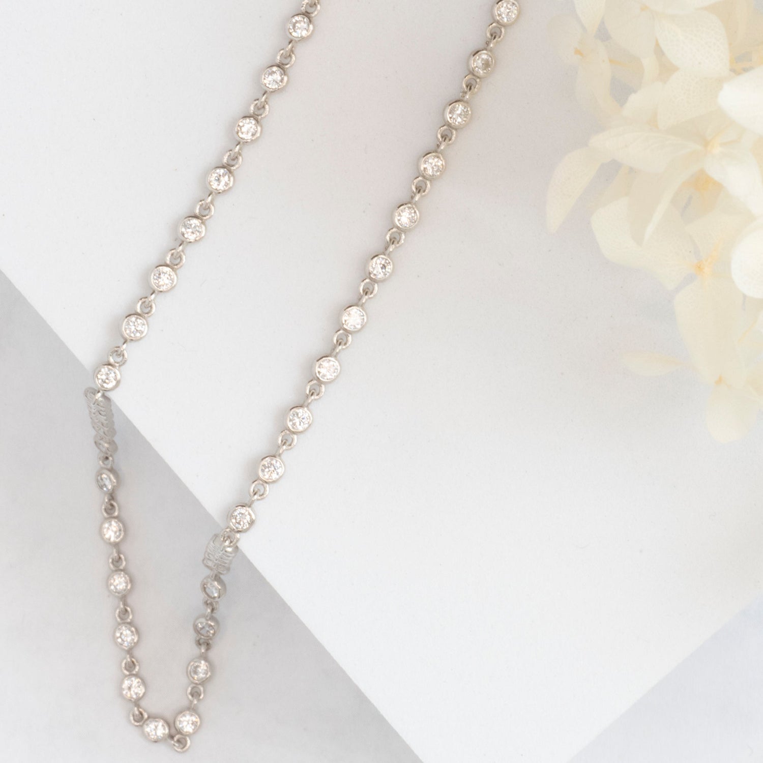 cubic zirconia chain necklace on white block with cream flowers