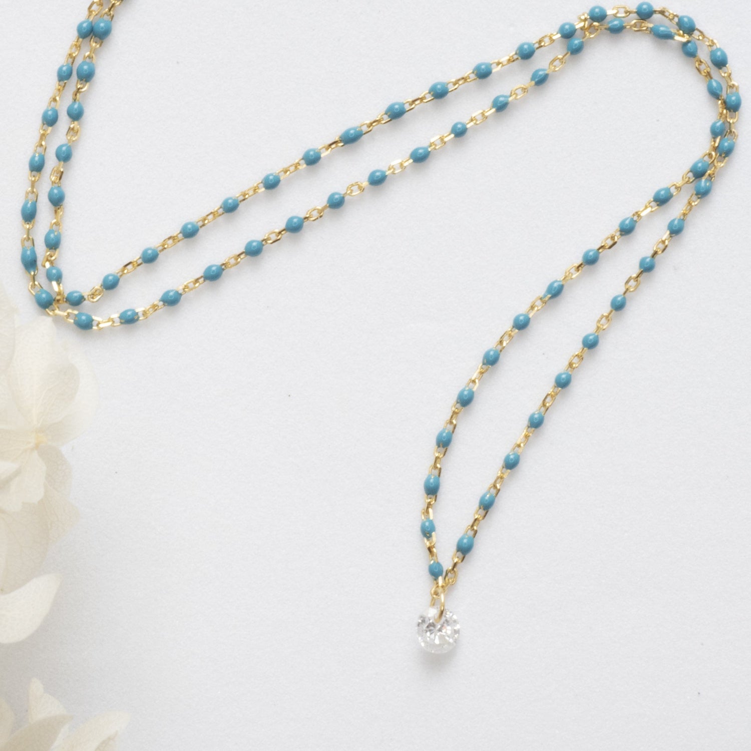 Cubic zirconia blue necklace laying flat on white background with flower