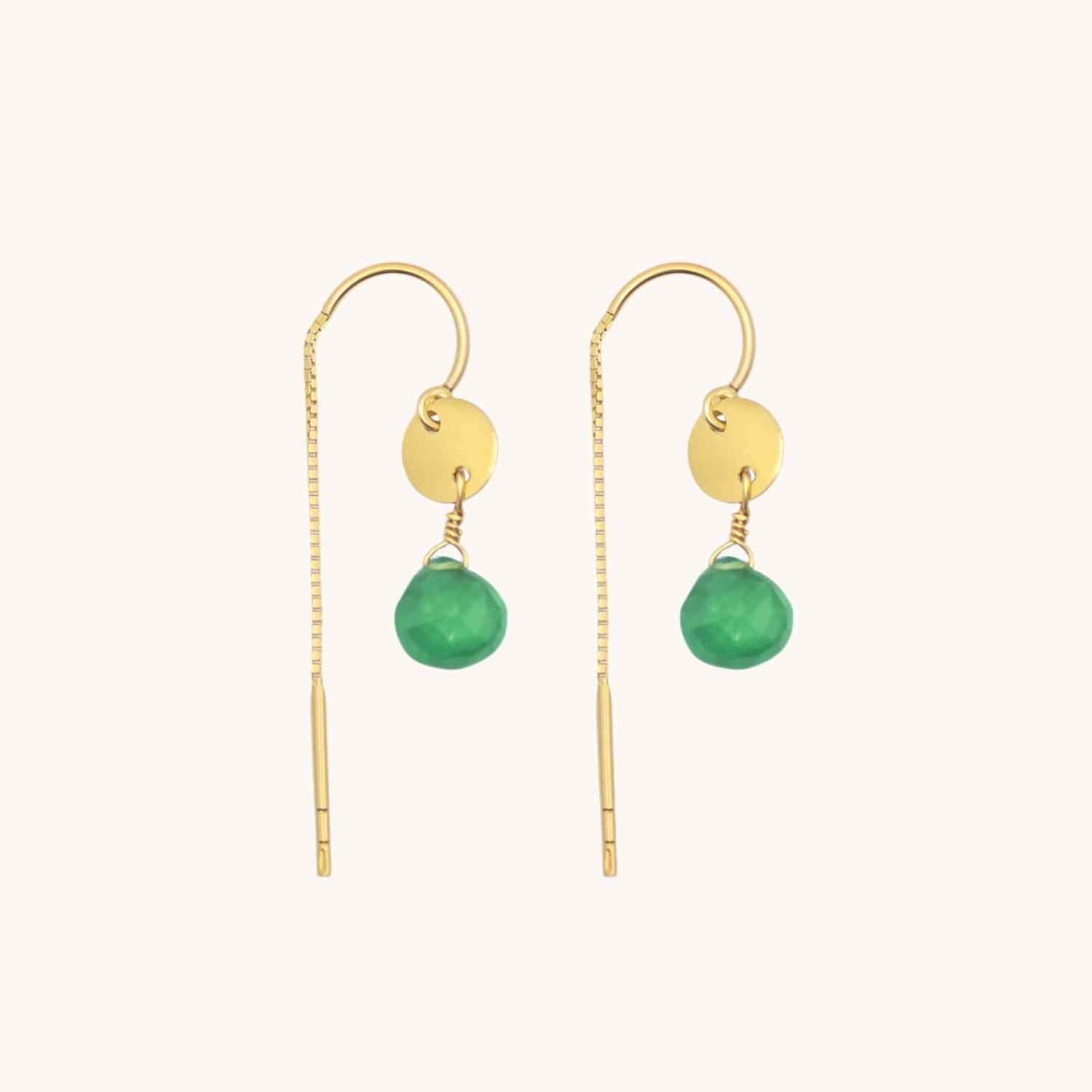Green drop gold earrings displayed on warm cream background