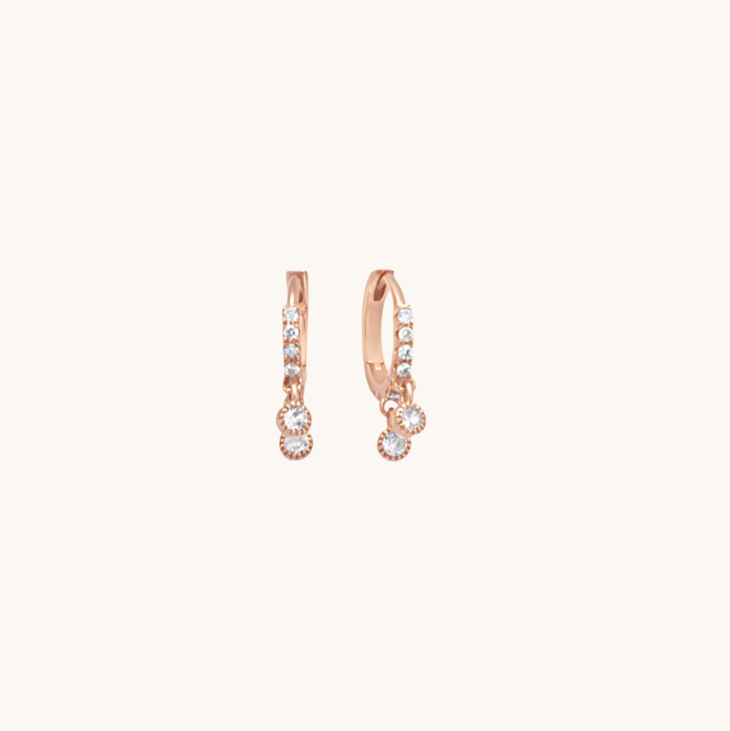 Rose gold huggy earrings with 2 cubic zirconia drops shown on cream background