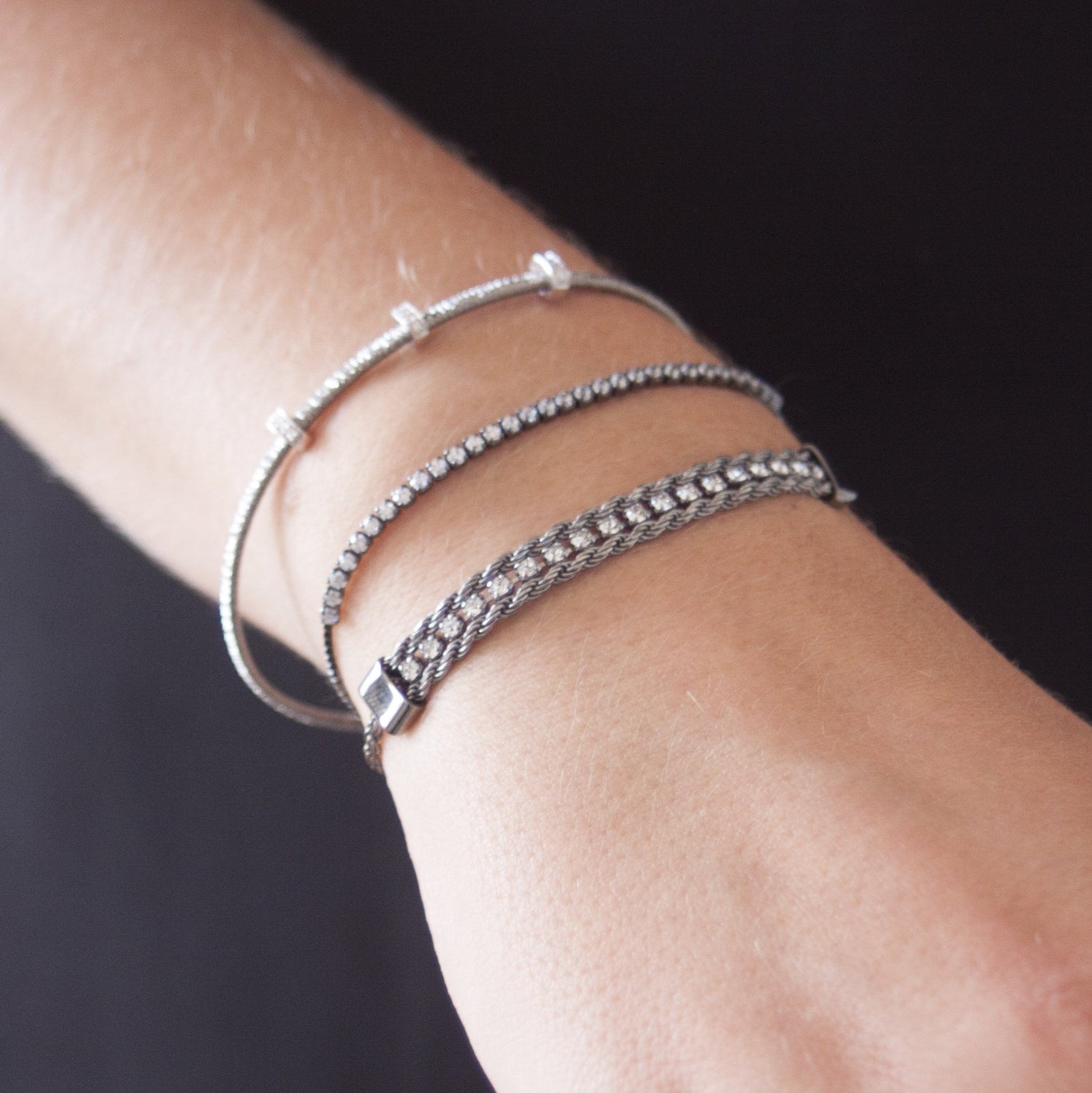 Model wearing a black tennis bracelet with cubic zirconia, stacked with other bracelets for a layered look.