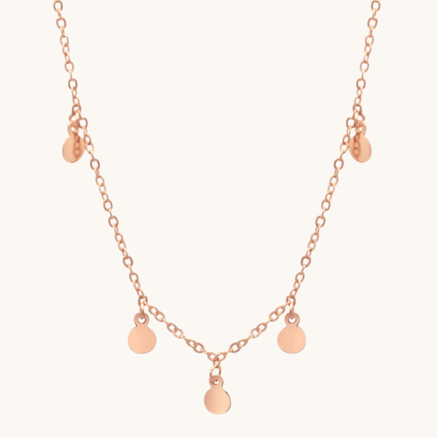 Rose gold boho necklace with small circle drops along its length, on cream background