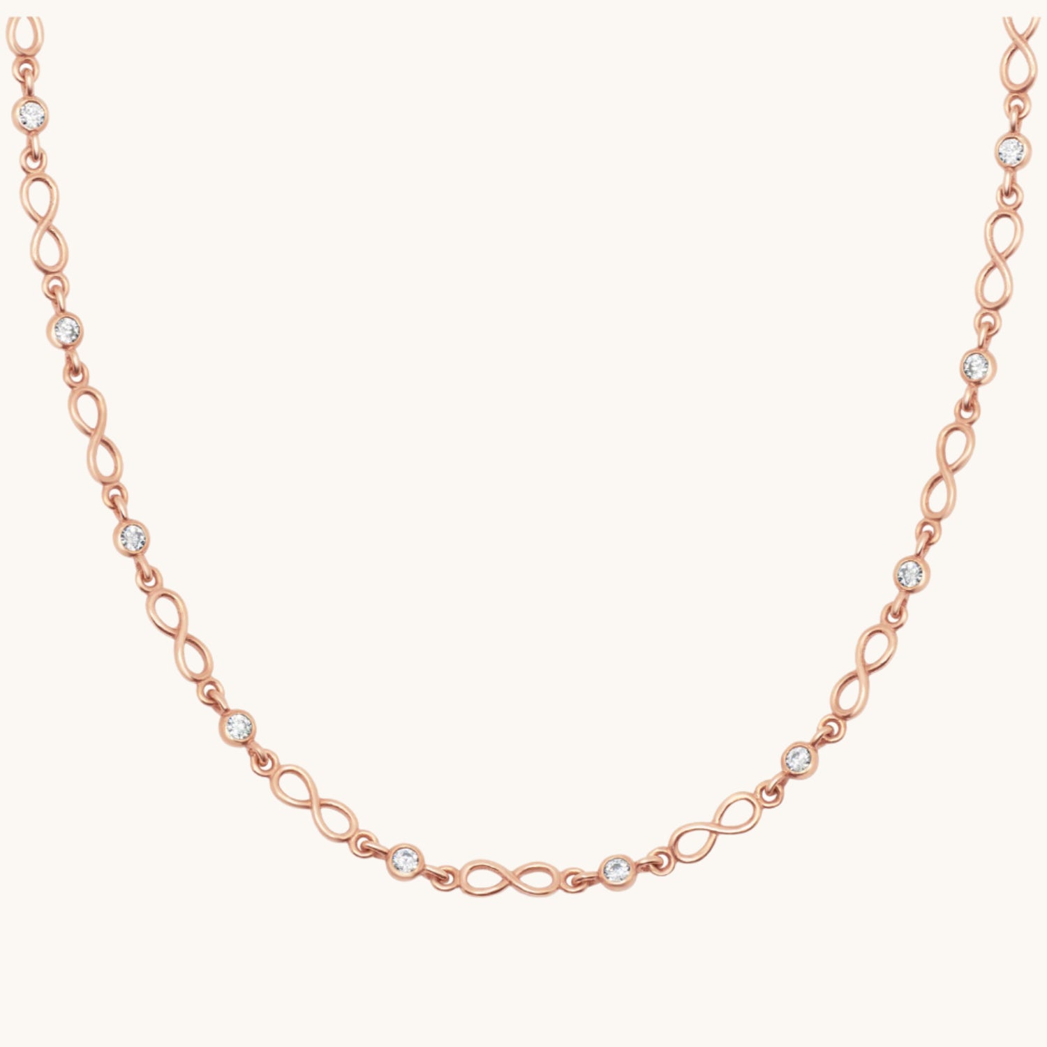 Rose gold infinity symbol necklace with cubic zirconia along chain, on cream background