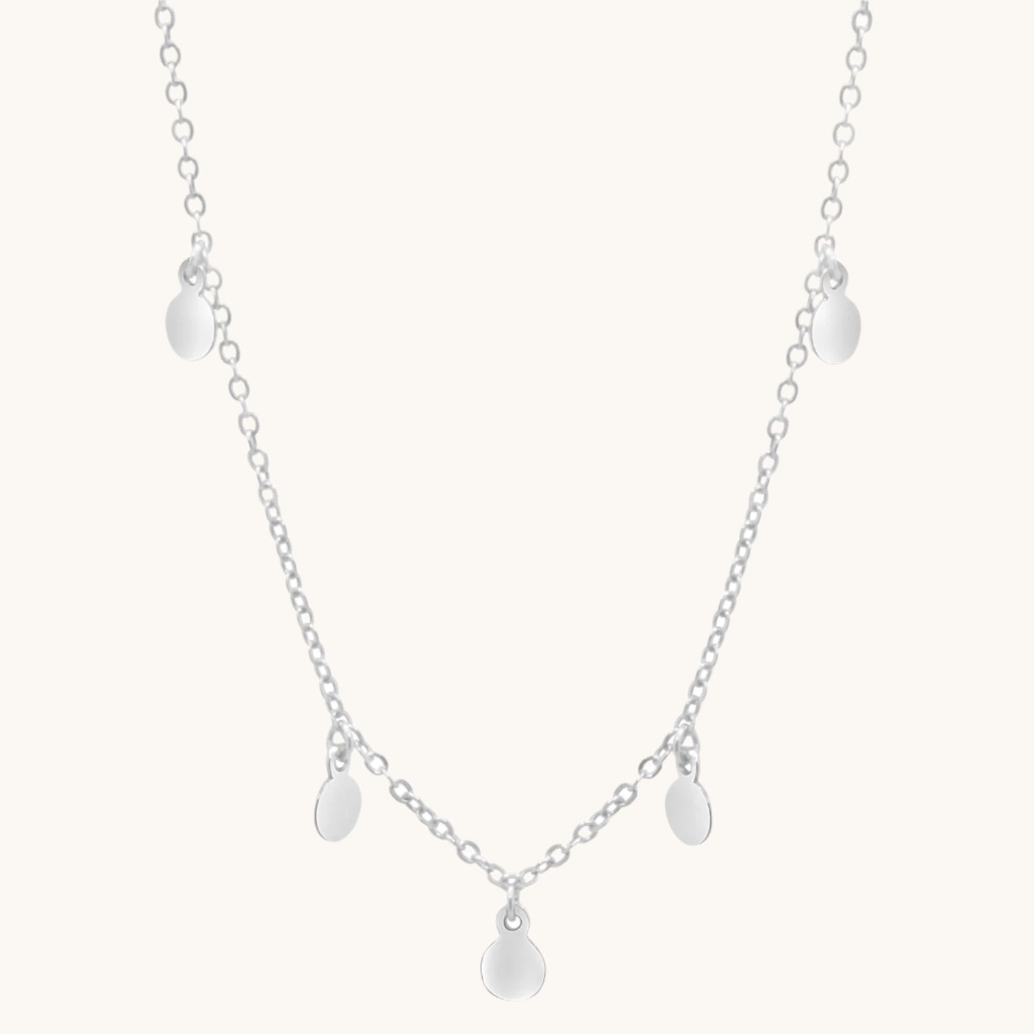 Sterling silver boho necklace with small circle drops along its length, on cream background