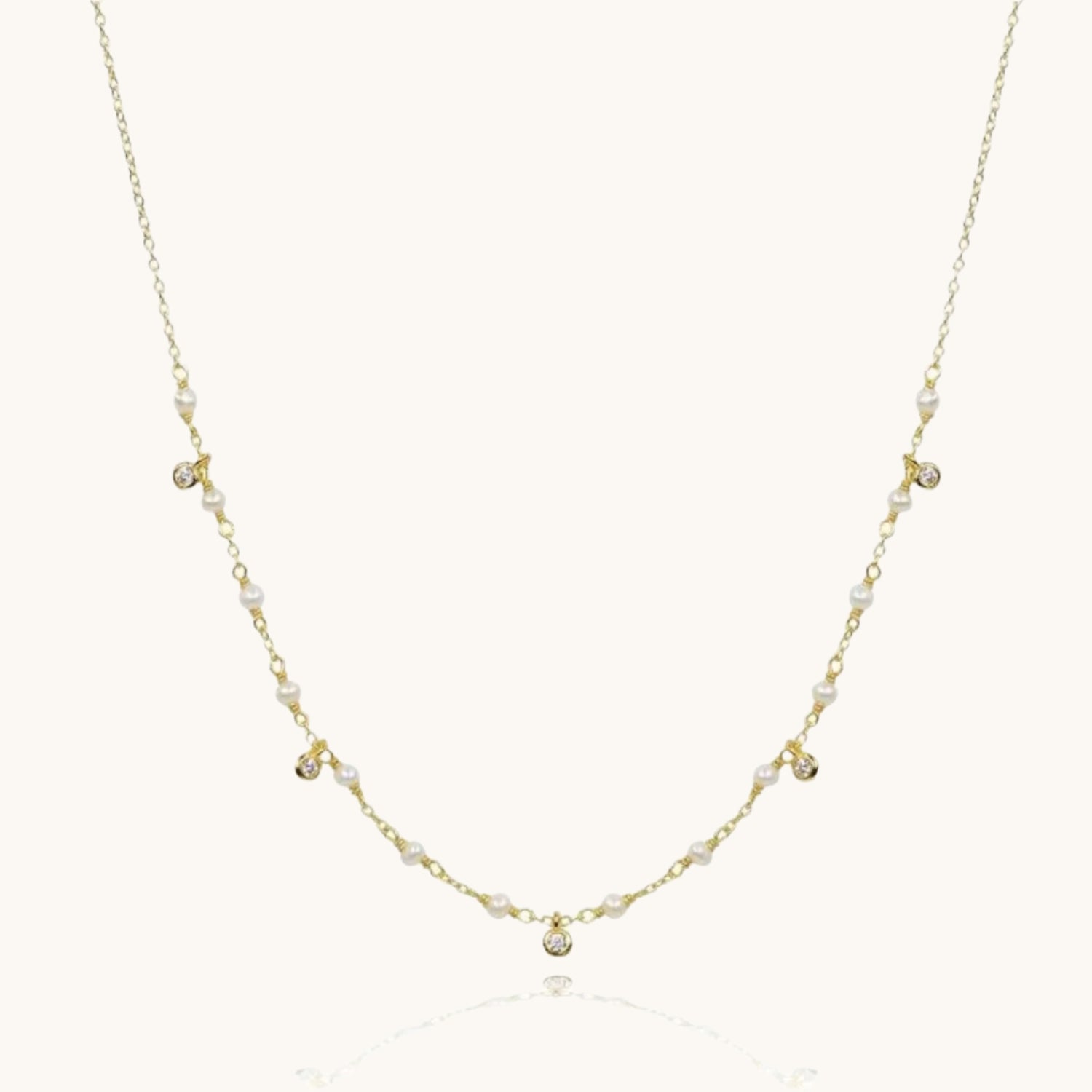 Cubic zirconia and pearl drop gold necklace on cream background