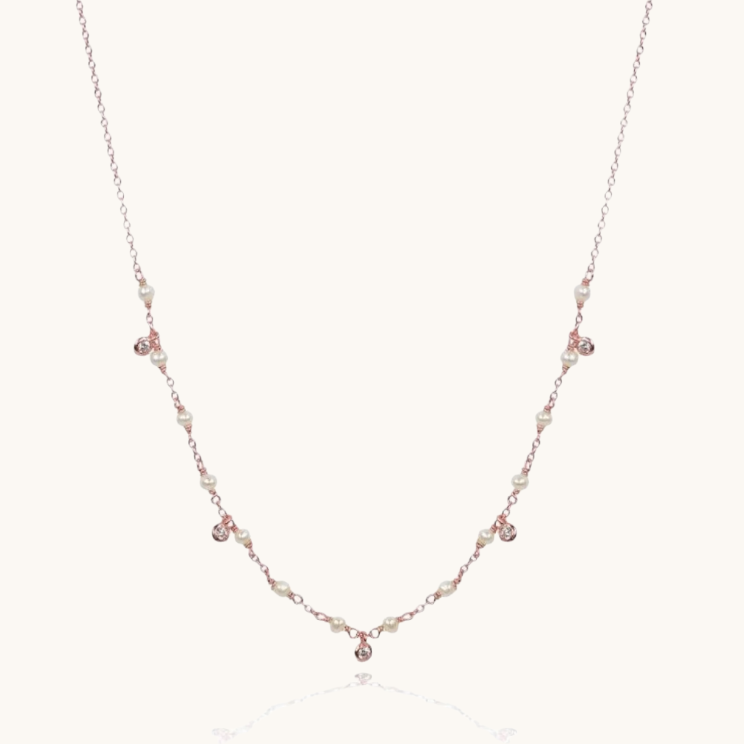 Cubic zirconia and pearl drop rose gold necklace on cream background